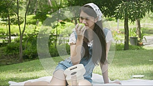 Beautiful young asian woman holding apple green and eating while relax in the park.