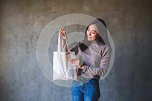 A beautiful young asian woman holding and carrying a white fabric tote bag for reusable and environment concept