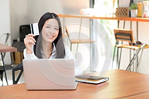 Beautiful young asian woman holding a credit card and shopping online with using laptop computer