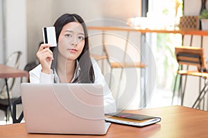 Beautiful young asian woman holding a credit card and shopping online with using laptop computer at cafe