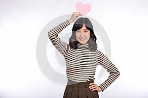 Beautiful young asian woman holding a paper heart while standing against white background. Beautiful young asian woman with paper