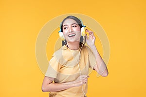 Beautiful young asian woman joyful listening to music on headphones isolated on pastel yellow wall background studio portrait