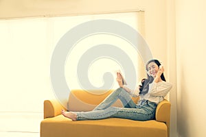 Beautiful young Asian woman listening music with headphones using a tablet on sofa in the room,