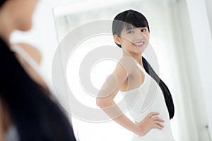 Beautiful young asian woman looking body in mirror with belly figure slim at home.