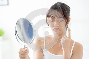 Beautiful young asian woman looking the mirror with acne problem at bedroom, trouble of beauty on face.