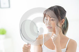 Beautiful young asian woman looking the mirror with acne problem at bedroom, trouble of beauty on face, zit treatment photo