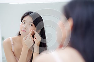 Beautiful young asian woman looking the mirror and touch face is a acne, zit treatment. photo