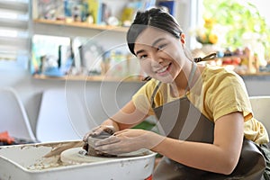Beautiful young asian woman making ceramic cup, moulding clay on a potter`s wheel