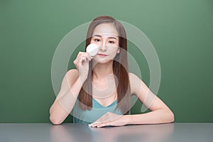 Beautiful young Asian woman with perfect skin removes make up with cotton pad, face cleaning concept