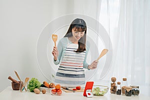 Beautiful young asian woman reading cooking recipe or watching show while making salad