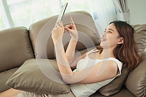 Beautiful young asian woman relax enjoy on the brown sofa and using digital tablet.