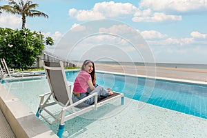 Beautiful young asian woman relaxing and sunbathing on lounge chair in swimming pool on tropical sea