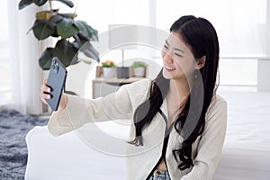 Beautiful young asian woman selfie with smartphone on social media in bedroom at home.