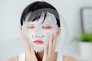 Beautiful young asian woman with sheet facial mask at home, beauty girl applying cosmetic and makeup with skin care.