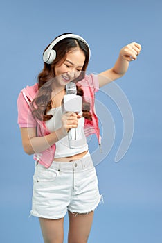 Beautiful young Asian woman singing into a microphone isolated over blue background