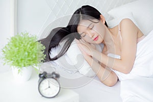 Beautiful young asian woman sleep with relax on the bed with alarm clock in the morning.