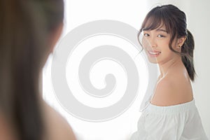 Beautiful young asian woman smiling with clothes trying on dressed up fitting with modern and looking reflect mirror in the room