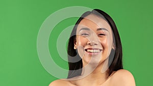 Beautiful young asian woman smiling and looking at camera isolated on green background