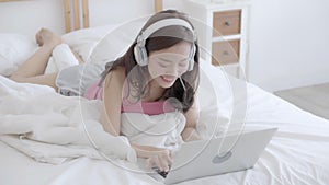 Beautiful young asian woman smiling say hello using chat social network with video call on laptop computer on bed at bedroom