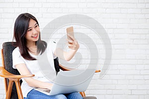 Beautiful young asian woman smiling and selfie with smartphone during work from home in living room.