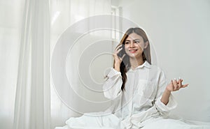 Beautiful young asian woman smiling sitting relax on the bed in the morning, girl using mobile smart phone talking enjoy