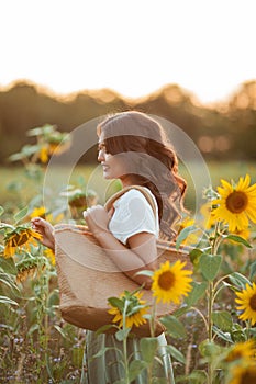 Beautiful young Asian woman in sunflower field at sunset. Model with dark long curly hair. Summer, sun