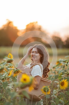 Beautiful young Asian woman in sunflower field at sunset. Model with dark long curly hair. Summer, sun