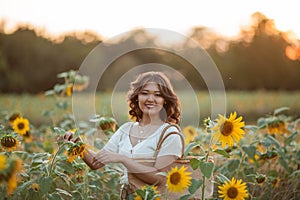 Beautiful young Asian woman in sunflower field at sunset. Model with dark long curly hair. Summer, sun