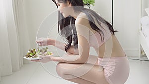 Beautiful young asian woman in underwear with figure perfect eating organic vegetable with salad for breakfast in the home