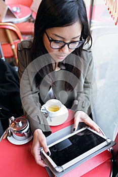 Beautiful young asian woman using her digital tablet while drinking coffee in coffee shop.