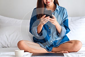 A beautiful young asian woman using mobile phone and laptop while sitting on a white bed