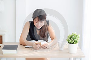 Beautiful young asian woman using touch smart mobile phone chatting message and notebook on desk.