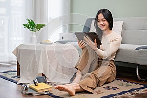 A beautiful Asian woman watching a movie on her digital tablet while relaxing in her living room