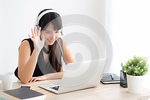 Beautiful young asian woman wear headphone smiling say hello using chat video call on laptop computer