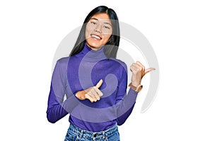 Beautiful young asian woman wearing casual clothes pointing to the back behind with hand and thumbs up, smiling confident