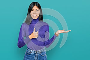 Beautiful young asian woman wearing casual clothes showing palm hand and doing ok gesture with thumbs up, smiling happy and