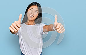 Beautiful young asian woman wearing casual white t shirt approving doing positive gesture with hand, thumbs up smiling and happy