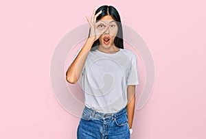 Beautiful young asian woman wearing casual white t shirt doing ok gesture shocked with surprised face, eye looking through fingers