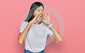 Beautiful young asian woman wearing casual white t shirt shouting angry out loud with hands over mouth