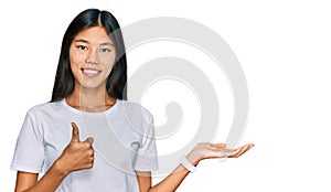 Beautiful young asian woman wearing casual white t shirt showing palm hand and doing ok gesture with thumbs up, smiling happy and