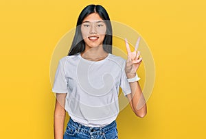 Beautiful young asian woman wearing casual white t shirt showing and pointing up with fingers number two while smiling confident