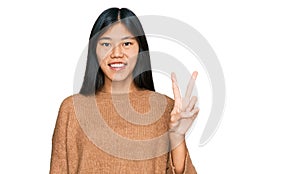 Beautiful young asian woman wearing casual winter sweater showing and pointing up with fingers number two while smiling confident