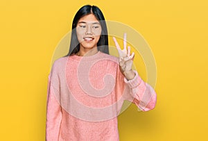 Beautiful young asian woman wearing casual winter sweater showing and pointing up with fingers number two while smiling confident