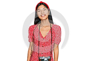 Beautiful young asian woman wearing dress and vintage camera looking positive and happy standing and smiling with a confident