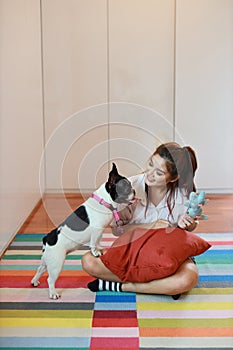 Beautiful young asian woman wearing white shirt and holding red pillow who sitting and playing with her cute dog with happy and