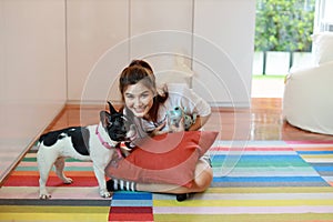 Beautiful young asian woman wearing white shirt and holding red pillow who sitting and playing with her cute dog with happy and