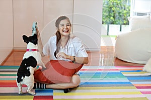 Beautiful young asian woman wearing white shirt and holding red pillow who sitting and playing with her cute dog with happy and