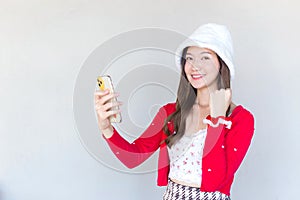 Beautiful young Asian woman who wears a red coat and white hat as a Santy girl holds a smartphone in her hand and another act