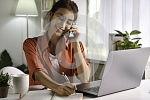 Beautiful young  Asian woman work at home with laptop and talking on smartphone and smiling. Female working on computer and using