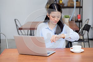 Krásny mladý ázijský žena pracovné na prenosný počítač v kaviareň hľadá na náramkové hodinky 